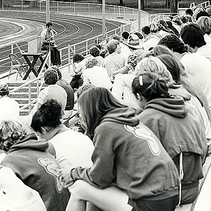 Black and white photo of CCS audience listening to a speaker on the track field.