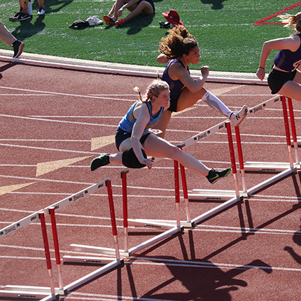 Sasquatch woman hurdler jumping over a hurdle against other opponent