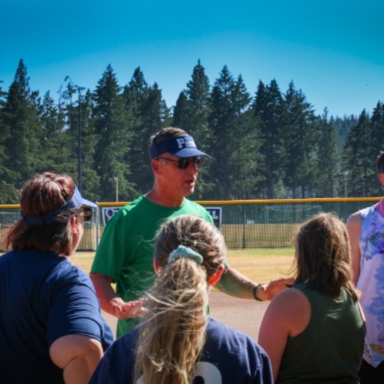 Pacers coach Jeff Dorney standing on the SFCC softball field with his team gathered around him, coaching his team.