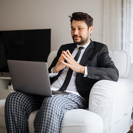 A man sitting in a suit top with tie and pajama bottoms with a laptop in his lap