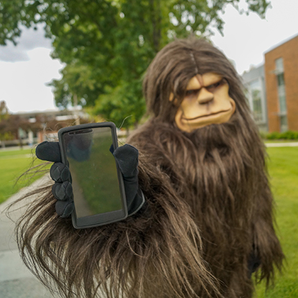 The SCC and SFCC Skitch mascot holding a smartphone