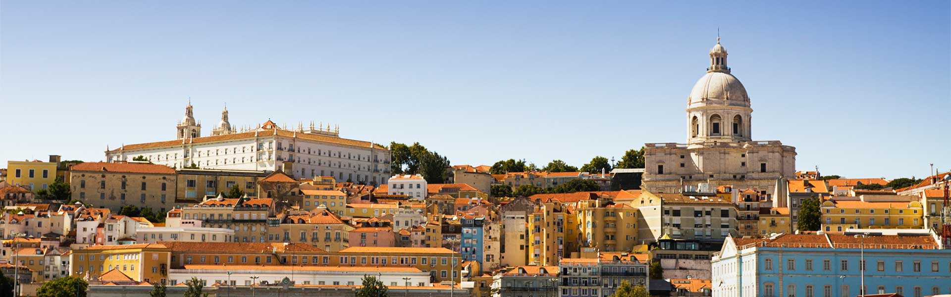 View of the Alfama district of Lisbon from the Tagus River with a clear blue sky overhead. 