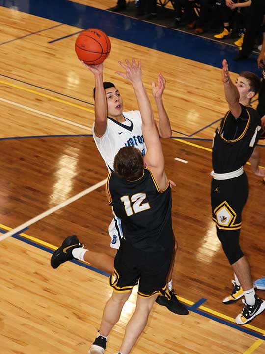 Men's basketball player in mid air going for the hoop surround two opponents