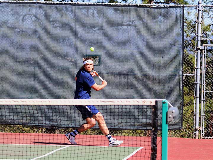 Men's tennis player hitting the ball with a back swing