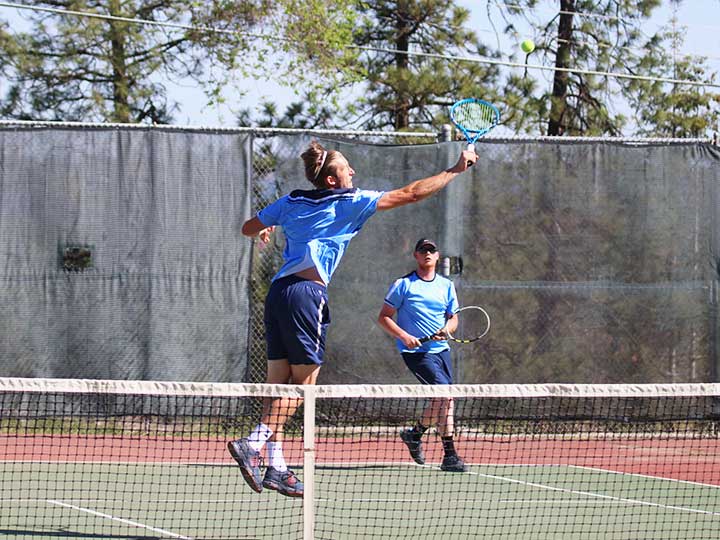 Men's tennis doubles player jumping to return the ball with a back swing