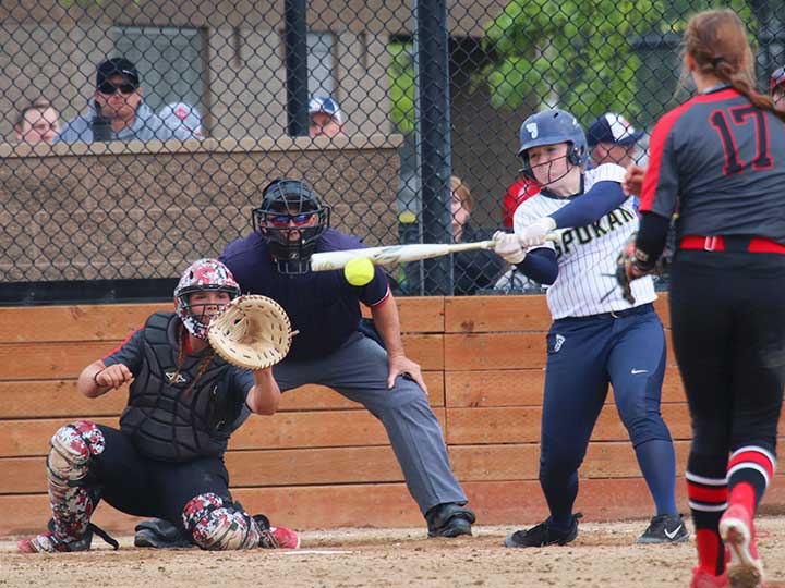 Softball player batting in mid swing with catcher in sight