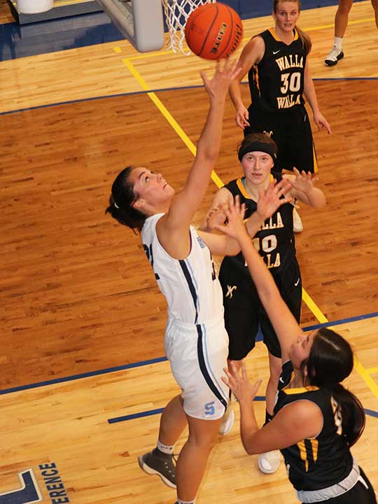 Women's Basketball player going for the layup backwards surrounded by opponents