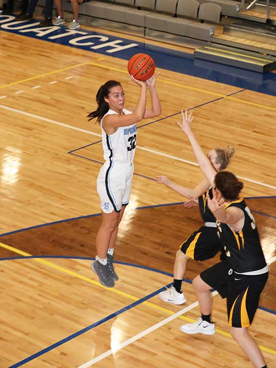 Women's basketball player in the air mid shoot on the hoop surrounded by opponents