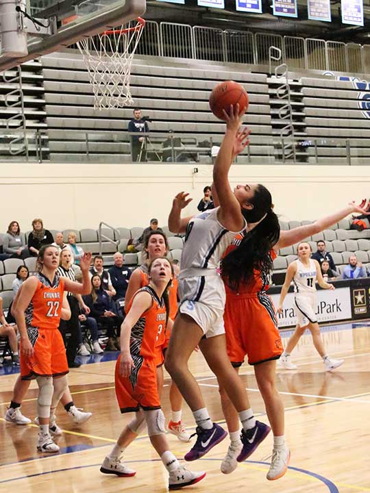 Women's basketball player jumping for the hoop while opponents watch