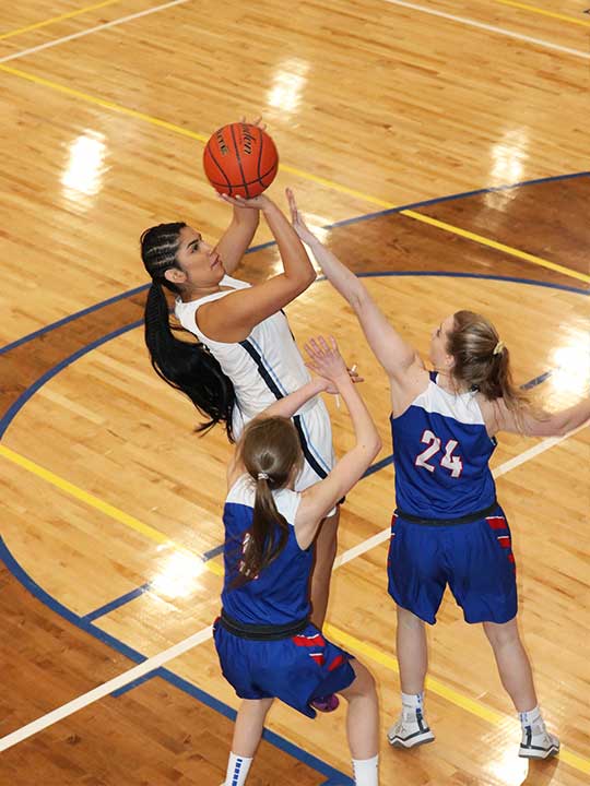 Women's Basketball player shooting for the hoop against two opponents.
