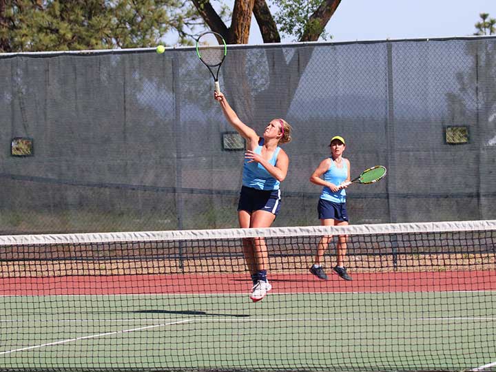 Women's tennis doubles player jumping to return the ball