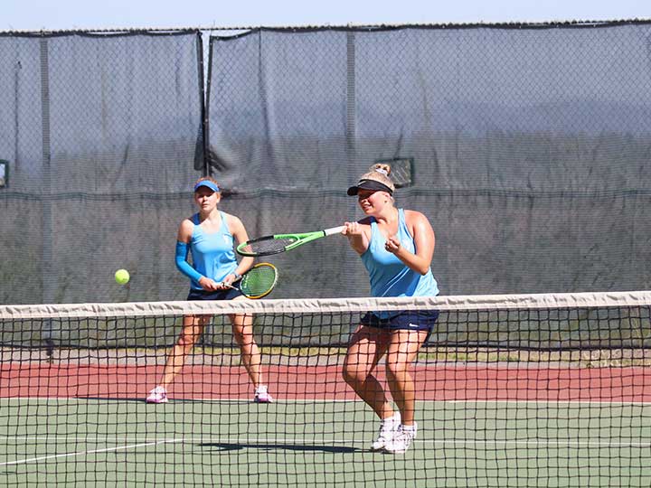 Women's tennis doubles player returning the ball with one hand underhand hit