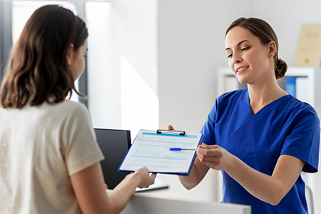 Medical office setting. Healthcare provider in blue scrubs handing a clipboard with a form to a person. 