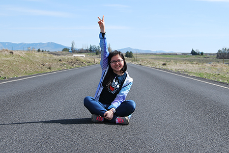 Angel Zian Chen sitting on a road giving the peace sign