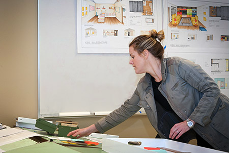 Interior design student organizing her work space with drawings hanging on the wall behind her.